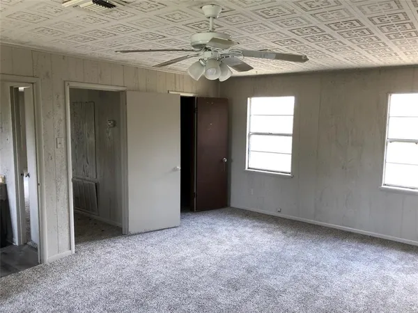 an empty room with a chandelier fan and windows