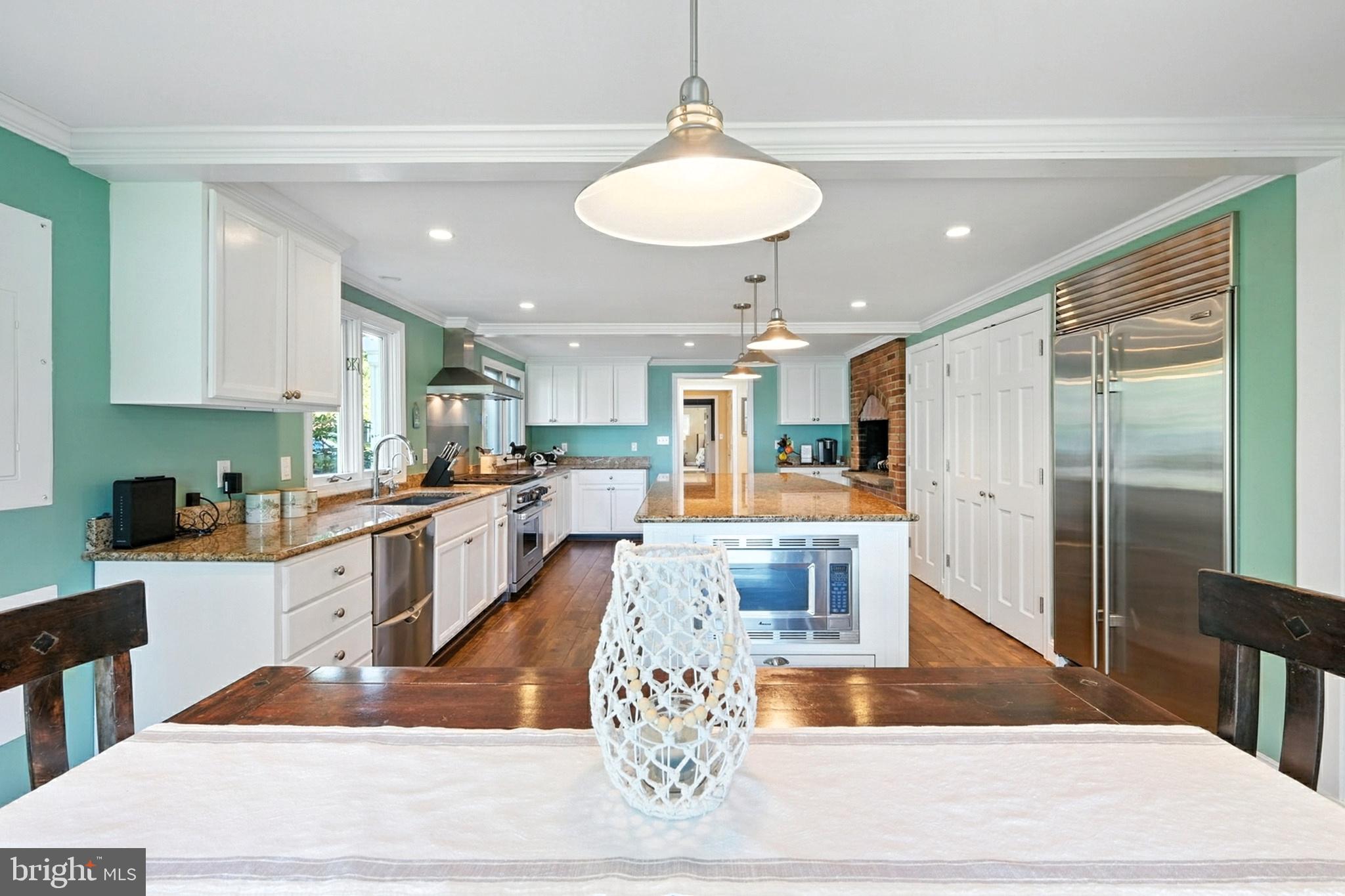 7312 Solitude Road St. Michaels, MD 21663 - Photo 20 of 43 a large white kitchen with kitchen island a refrigerator a stove a sink a dining table and chairs