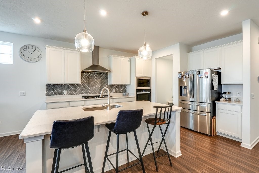 Kitchen with wall chimney exhaust hood, stainless steel fridge, a center island with sink, backsplash, and dark hardwood / wood-style flooring
