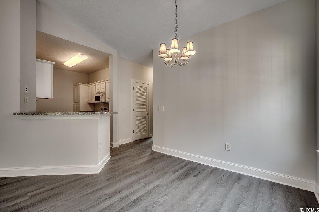 999 Algonquin Drive, Unit E Pawleys Island, SC 29585 - Photo 12 of 37 Unfurnished dining area with a notable chandelier, wood finished floors, and baseboards