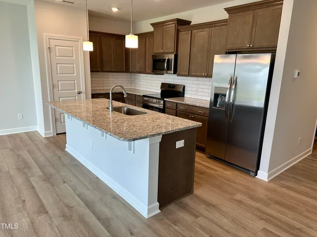 a kitchen with stainless steel appliances granite countertop a sink a refrigerator and wooden floor