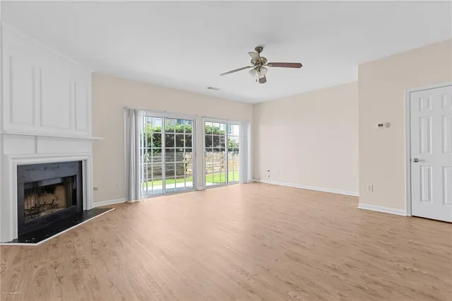 a view of an empty room with wooden floor fireplace and a window