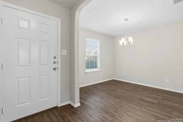 an empty room with wooden floor chandelier and windows