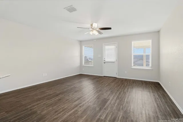an empty room with wooden floor ceiling fan and windows
