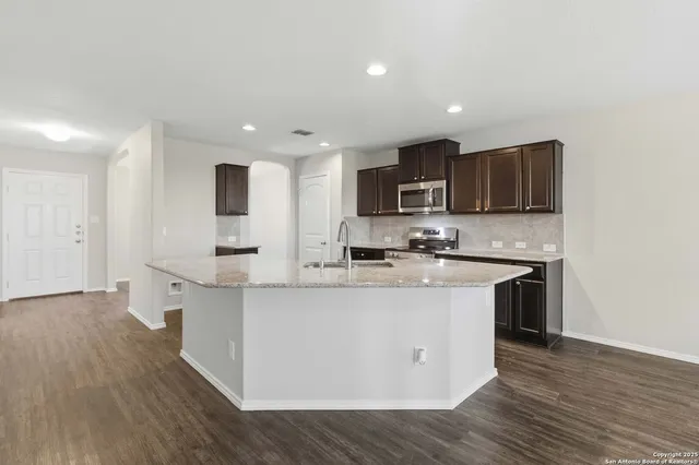 a large kitchen with stainless steel appliances granite countertop a stove top oven a sink a refrigerator and white cabinets with wooden floor