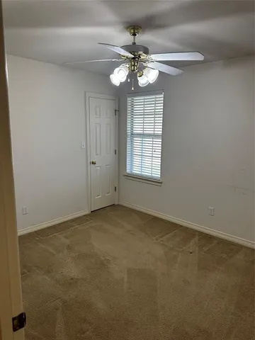an empty room with chandelier fan and windows