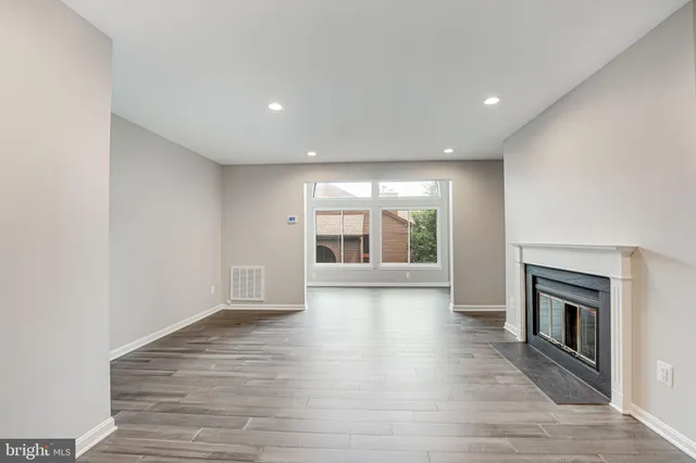 an empty room with wooden floor fireplace and windows