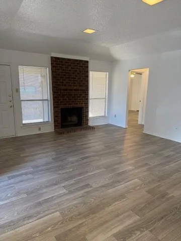 an empty room with wooden floor fireplace and windows