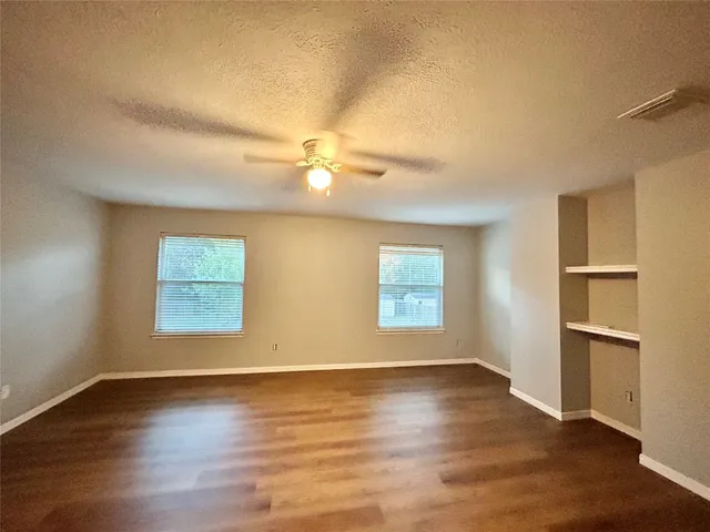 a view of empty room with wooden floor and fan