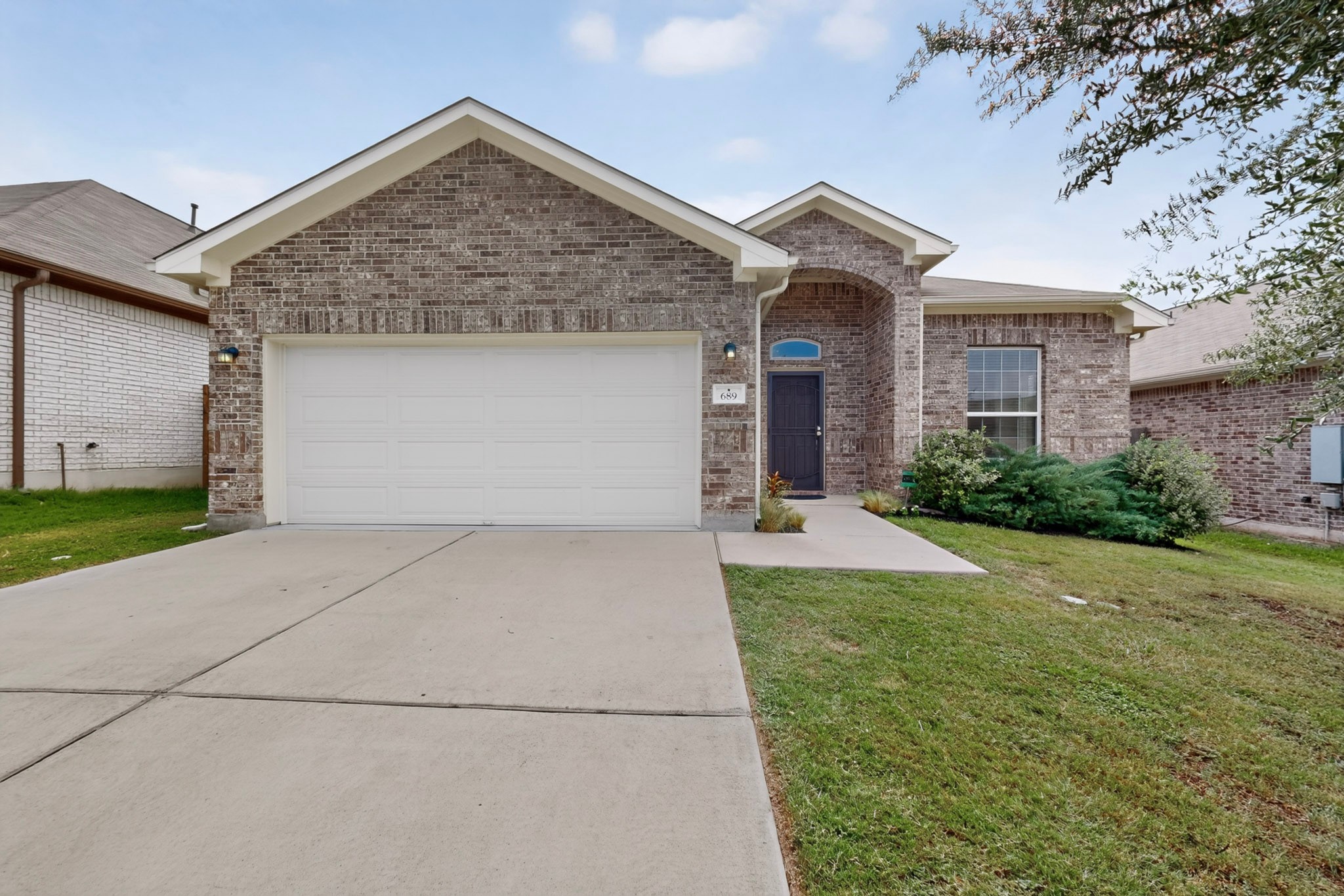 An inviting classic brick facade pairs with a neat concrete driveway and green lawn.