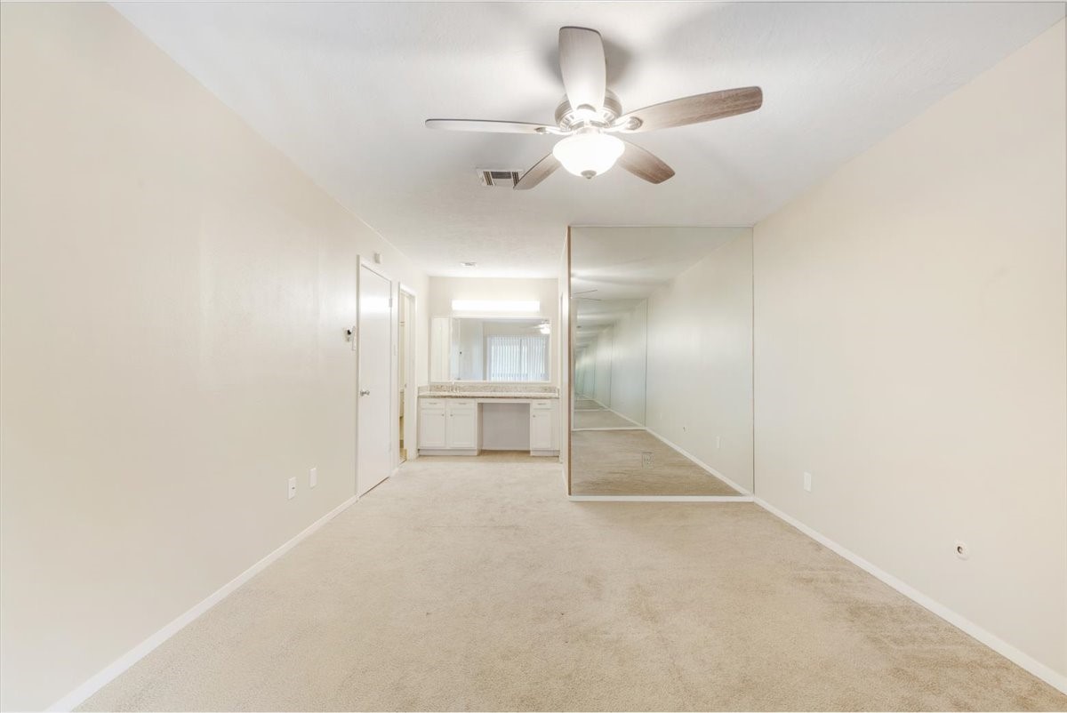 3502 Ocee Street, Unit 3502 Houston, TX 77063 - Photo 16 of 28 This room features a neutral carpet and walls, a ceiling fan, and a built-in vanity with a large mirror, creating a bright and spacious feel.