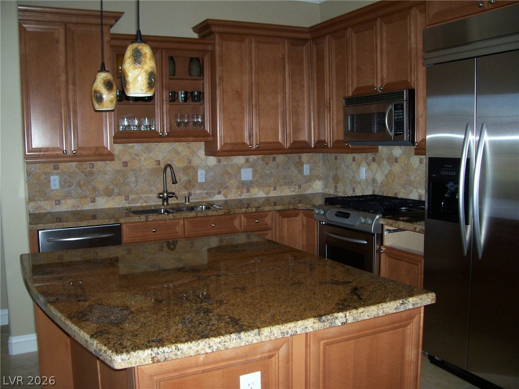 6 Via Vasari, Unit 104 Henderson, NV 89011 - Photo 4 of 13 Kitchen with appliances with stainless steel finishes, light stone countertops, backsplash, brown cabinetry, and decorative light fixtures