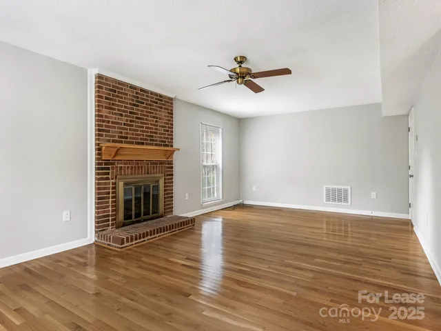 a view of an empty room with wooden floor and a fireplace