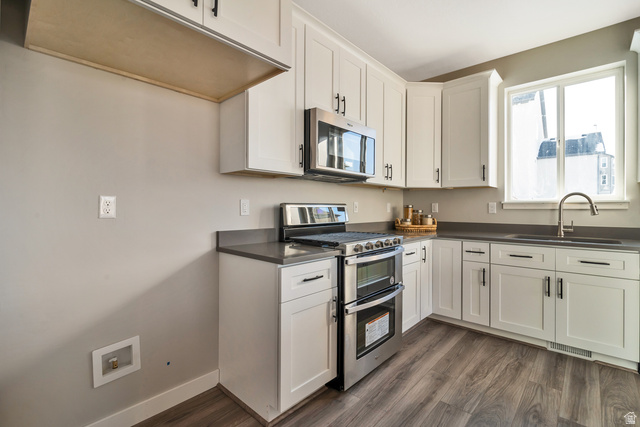 2449 Scarlet Road, Unit 249 Eagle Mountain, UT 84005 - Photo 19 of 26 White shaker-style cabinetry, stainless steel appliances, dark countertops, a stainless steel sink with a gooseneck faucet, and wood-finish flooring