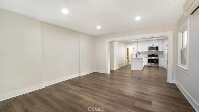a view of empty room with wooden floor and kitchen