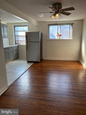 an empty room with wooden floor a kitchen view and windows