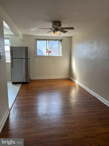 an empty room with wooden floor kitchen view and windows