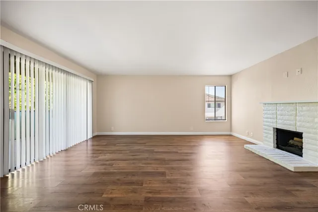 an empty room with wooden floor fireplace and windows