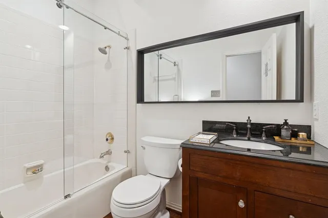a bathroom with a granite countertop sink a toilet a mirror a vanity and shower