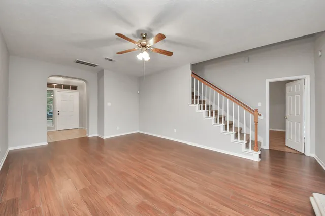 a view of an empty room with wooden floor and a chandelier fan