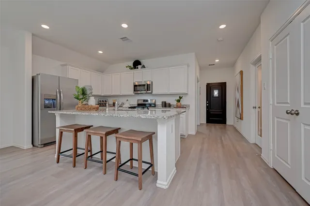 a kitchen with stainless steel appliances a dining table chairs refrigerator and cabinets