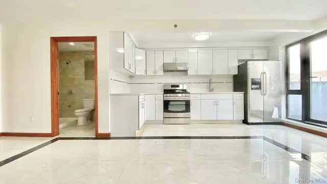 a kitchen with stainless steel appliances granite countertop a refrigerator a stove a sink and white cabinets with wooden floor