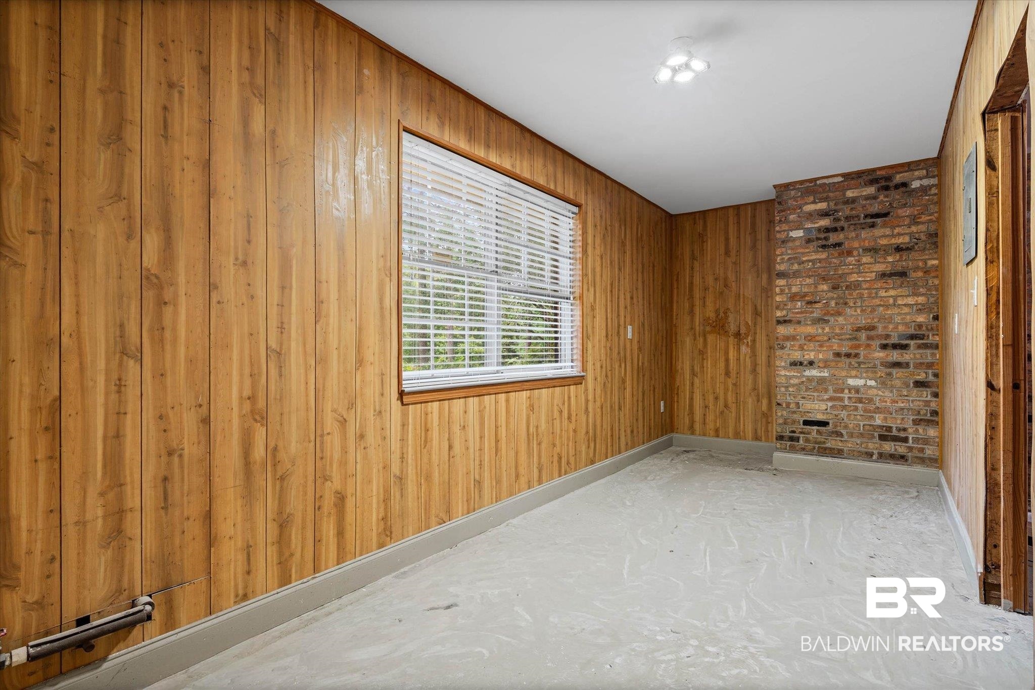 8301 Fordham Road Mobile, AL 36619 - Photo 28 of 57 Room featuring wood paneling, a brick accent wall, white window blinds, and a multi-bulb ceiling fixture