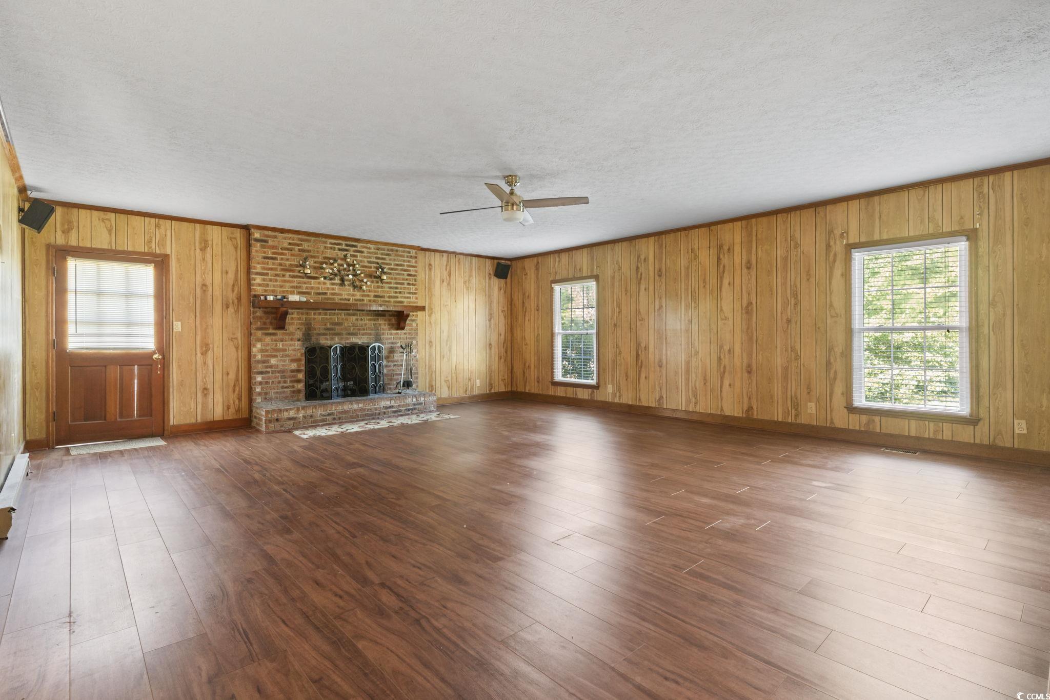 6971 Alfred Road Aynor, SC 29511 - Photo 7 of 37 Unfurnished living room featuring a brick fireplace, wood finished floors, wooden walls, a ceiling fan, and a textured ceiling