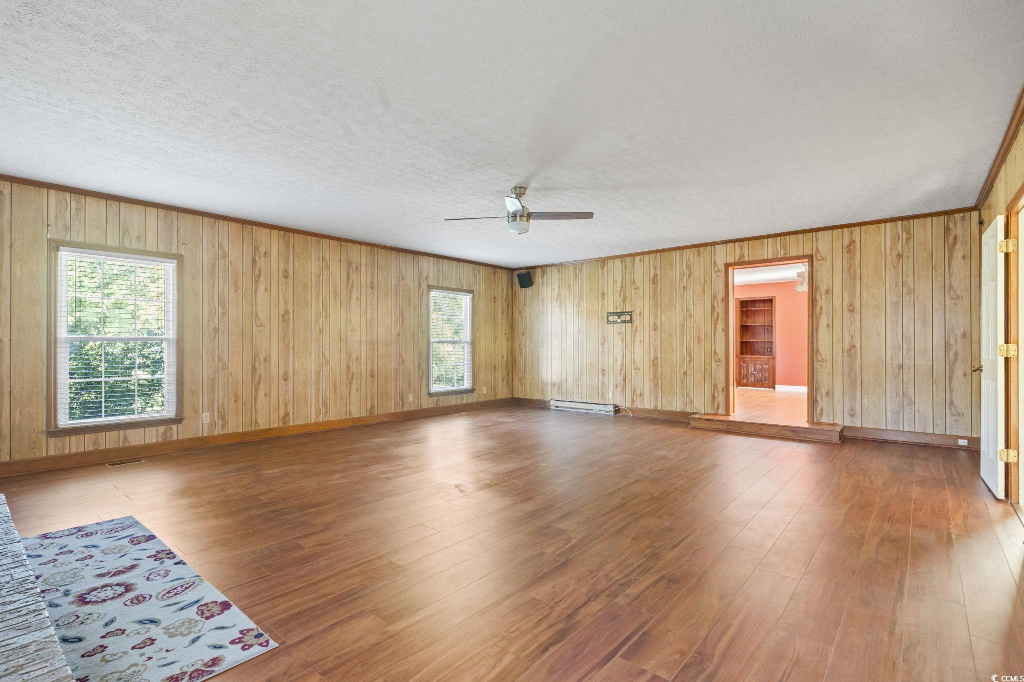 6971 Alfred Road Aynor, SC 29511 - Photo 9 of 37 Unfurnished room with wood finished floors, wooden walls, baseboard heating, ornamental molding, and ceiling fan
