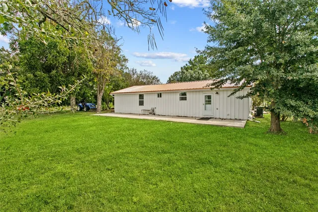 a view of a white house with a big yard and large trees