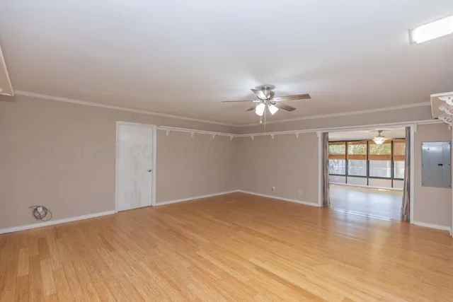 an empty room with wooden floor chandelier fan and windows
