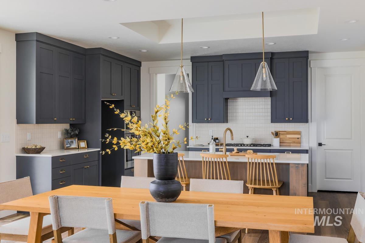 6091 South Apex Avenue Meridian, ID 83642 - Photo 12 of 40 Kitchen with a center island with sink, pendant lighting, backsplash, black refrigerator, and light stone counters