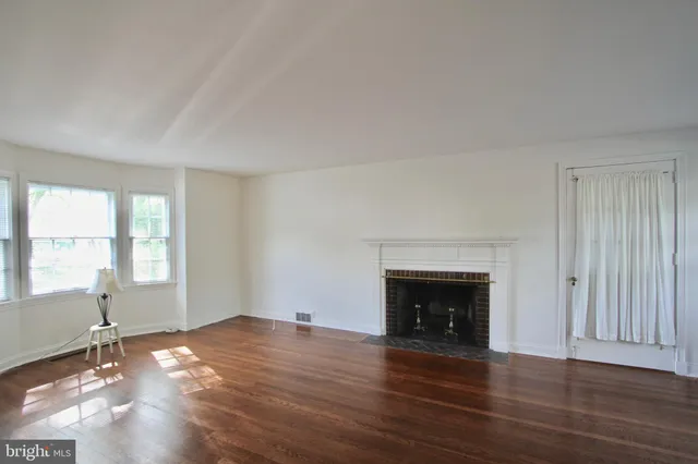 an empty room with wooden floor fireplace and windows