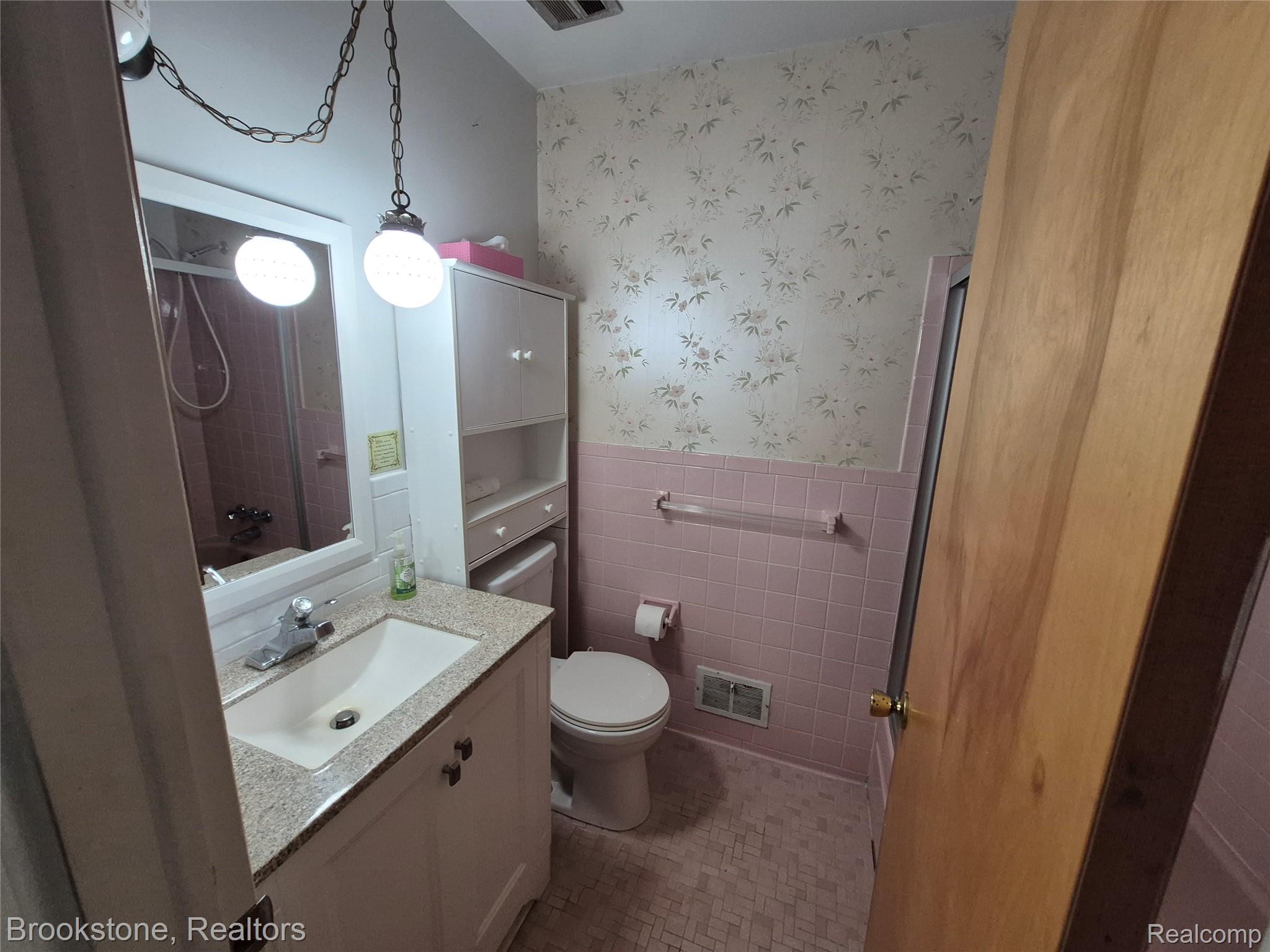 4295 Sashabaw Road Waterford, MI 48329 - Photo 25 of 37 Bathroom featuring a white vanity with a granite-style countertop and an integrated sink, a toilet, pink wall tiling, and a built-in storage cabinet