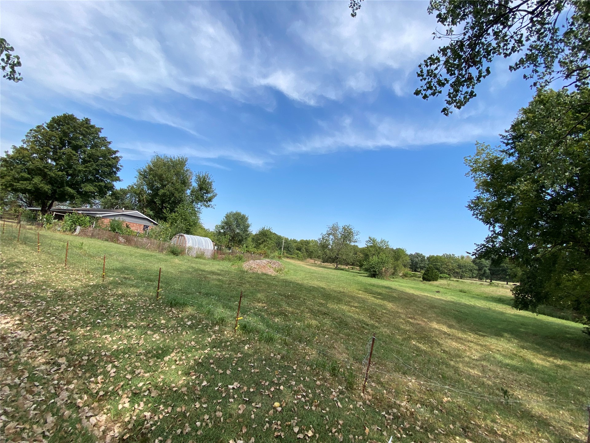 11131 215th Road Nowata, OK 74048 - Photo 35 of 47 From far SE corner front of property looking NE towards home and land Expansive green space featuring a gentle slope, mature trees, and a distant structure with a greenhouse