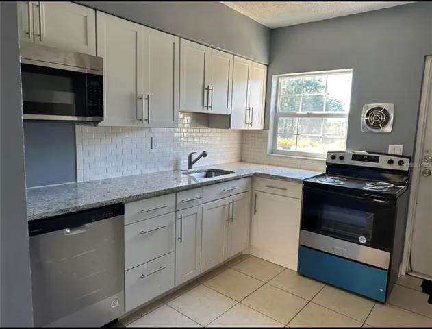 a kitchen with granite countertop white cabinets stainless steel appliances and a window