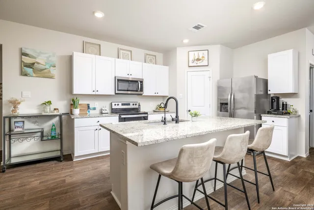 a kitchen with stainless steel appliances granite countertop a stove top oven a sink a refrigerator with a dining table and chairs