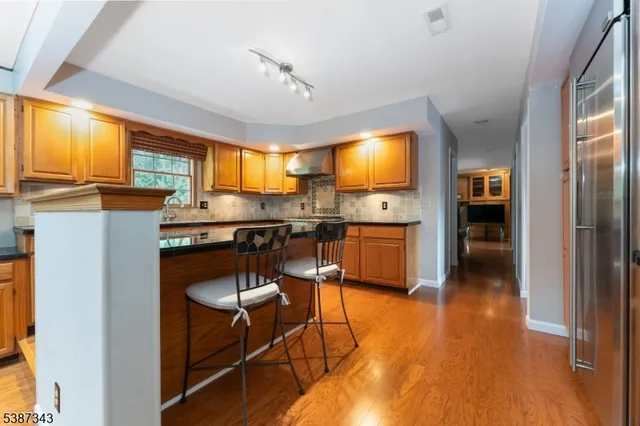 a kitchen with stainless steel appliances granite countertop a stove top oven a refrigerator a dining table and chairs with wooden floor