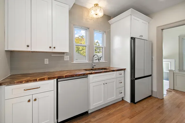 a kitchen with stainless steel appliances granite countertop a refrigerator a sink and white cabinets with wooden floor