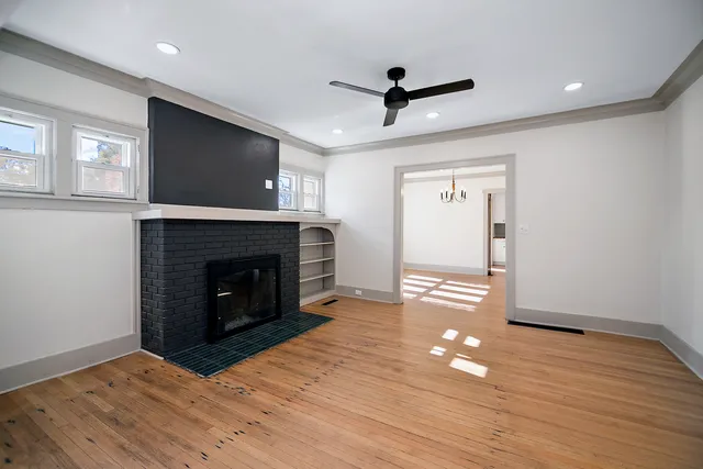 a view of a livingroom with a fireplace a ceiling fan and wooden floor
