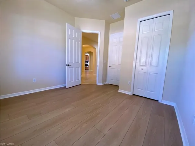 an empty room with wooden floor chandelier fan and windows