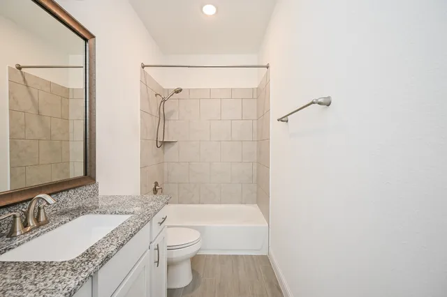 a bathroom with a granite countertop sink a toilet and shower