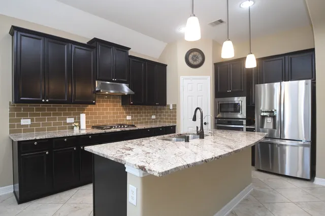 a kitchen with granite countertop kitchen island stainless steel appliances a sink stove and refrigerator