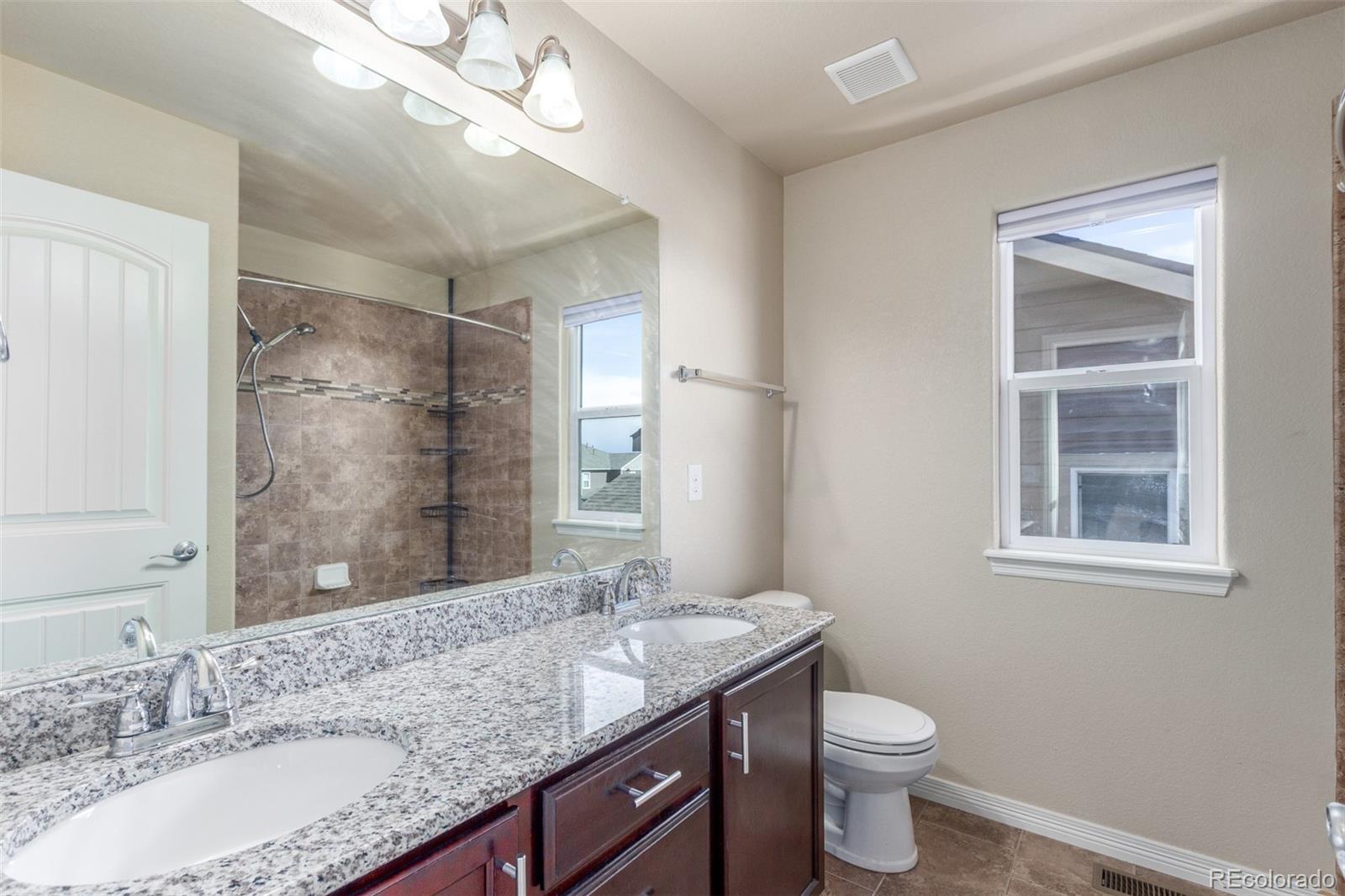 6654 12th Street Frederick, CO 80530 - Photo 27 of 50 a bathroom with a granite countertop sink a toilet a mirror and shower