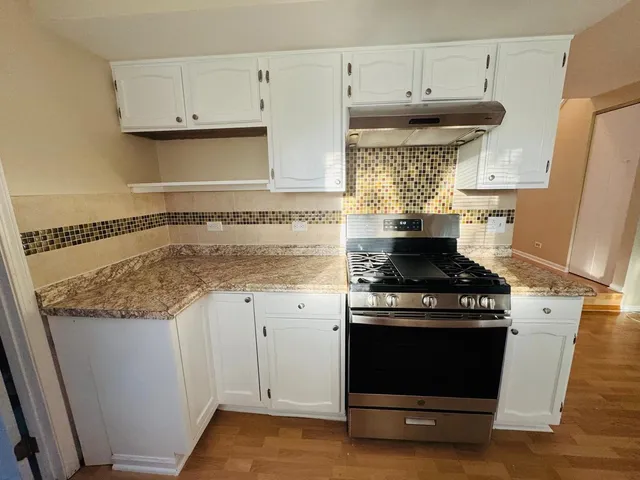 a kitchen with granite countertop a stove and white cabinets