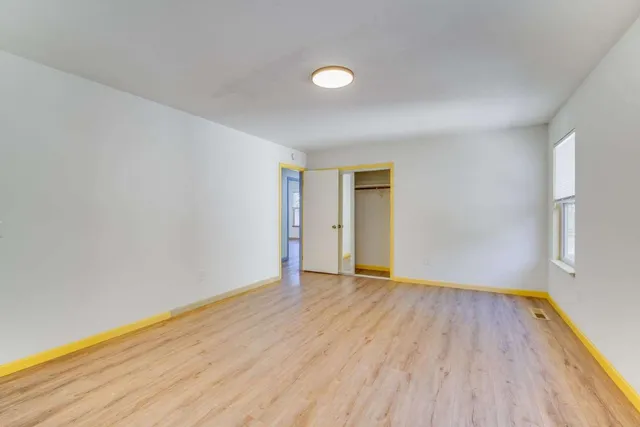 a view of an empty room with wooden floor and a window