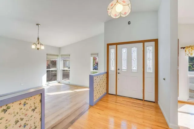 a view of an empty room and kitchen view with wooden floor
