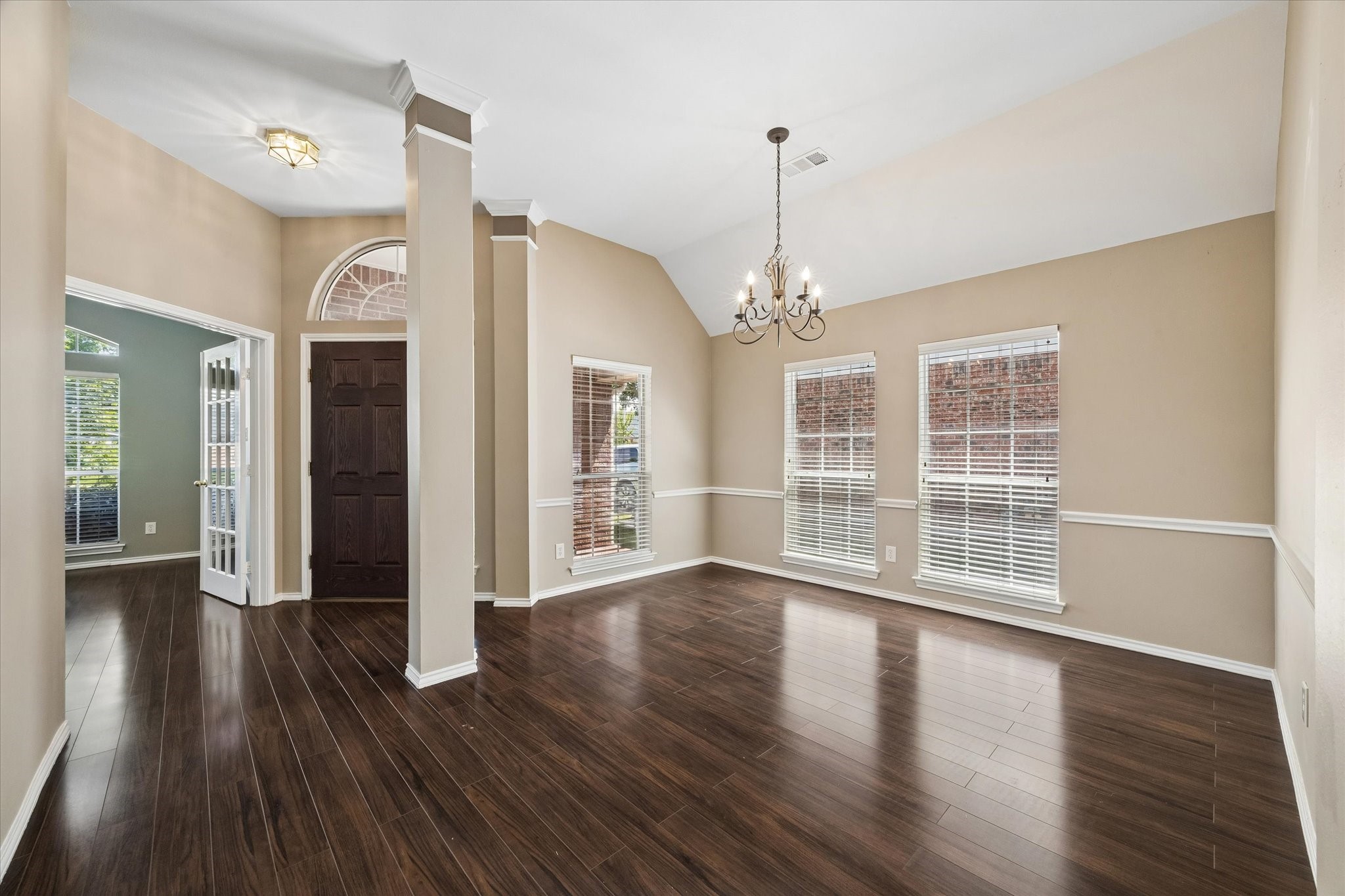 3118 Valley Court Manvel, TX 77578 - Photo 24 of 38 This photo showcases a bright, open living space with elegant hardwood floors, neutral walls, and a classic chandelier. Large windows provide plenty of natural light, while a dark wood front door adds a touch of sophistication. The adjoining room through French doors enhances the open feel.