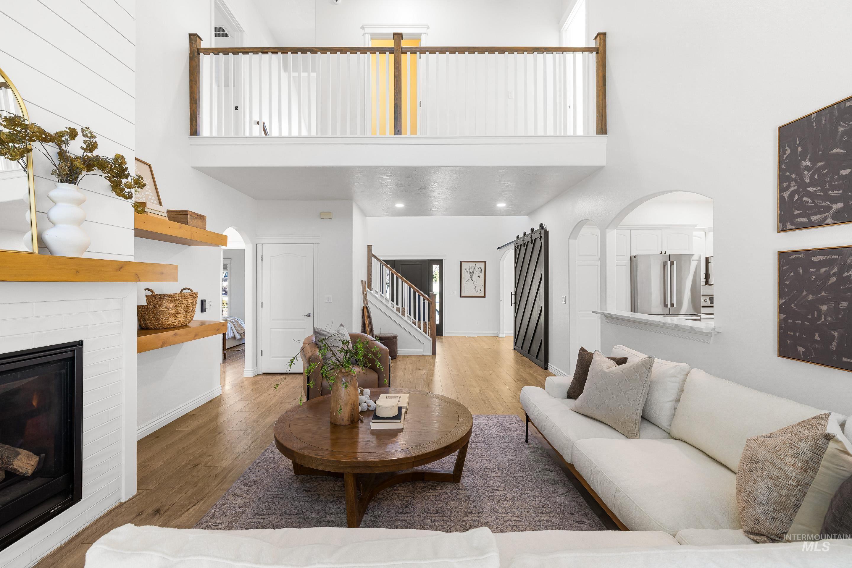 1197 North Cove Colony Way Eagle, ID 83616 - Photo 7 of 50 Living room with a towering ceiling, a glass covered fireplace, wood finished floors, stairway, and arched walkways