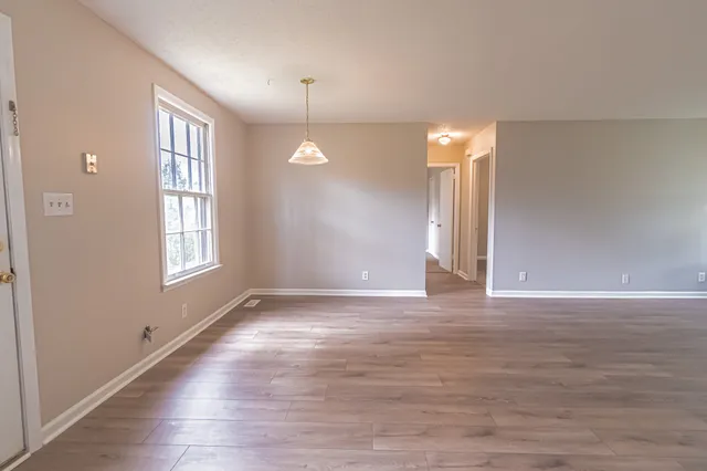 a view of an empty room with window and hardwood floor